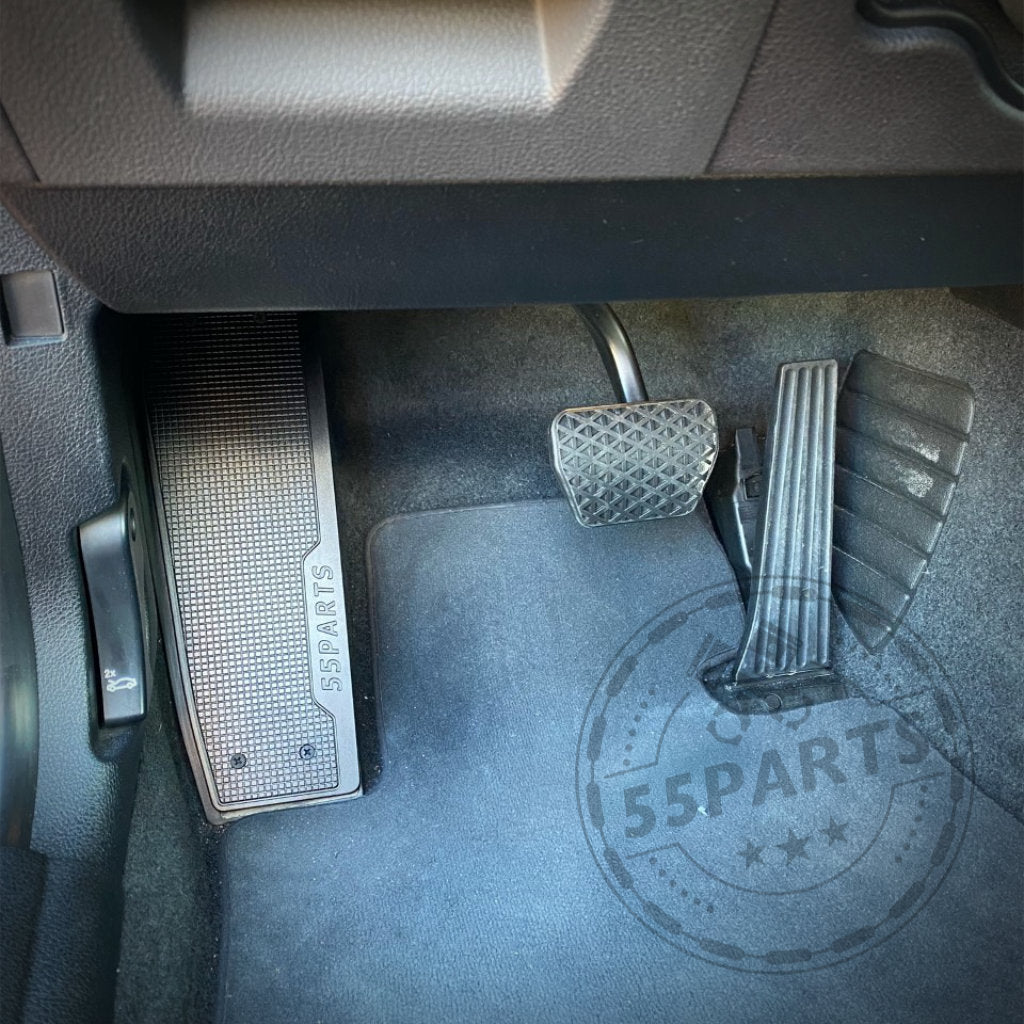 Fahrzeugboden mit Gas-, Brems- und Kupplungspedalen, einem BMW-Fußraum und einer 55Parts-Spezial-Aluminium-Fußstützen-Fußablage mit 55Parts-Logo für die Modelle F2x, F3x und F8x sowie einer Fußmatte.