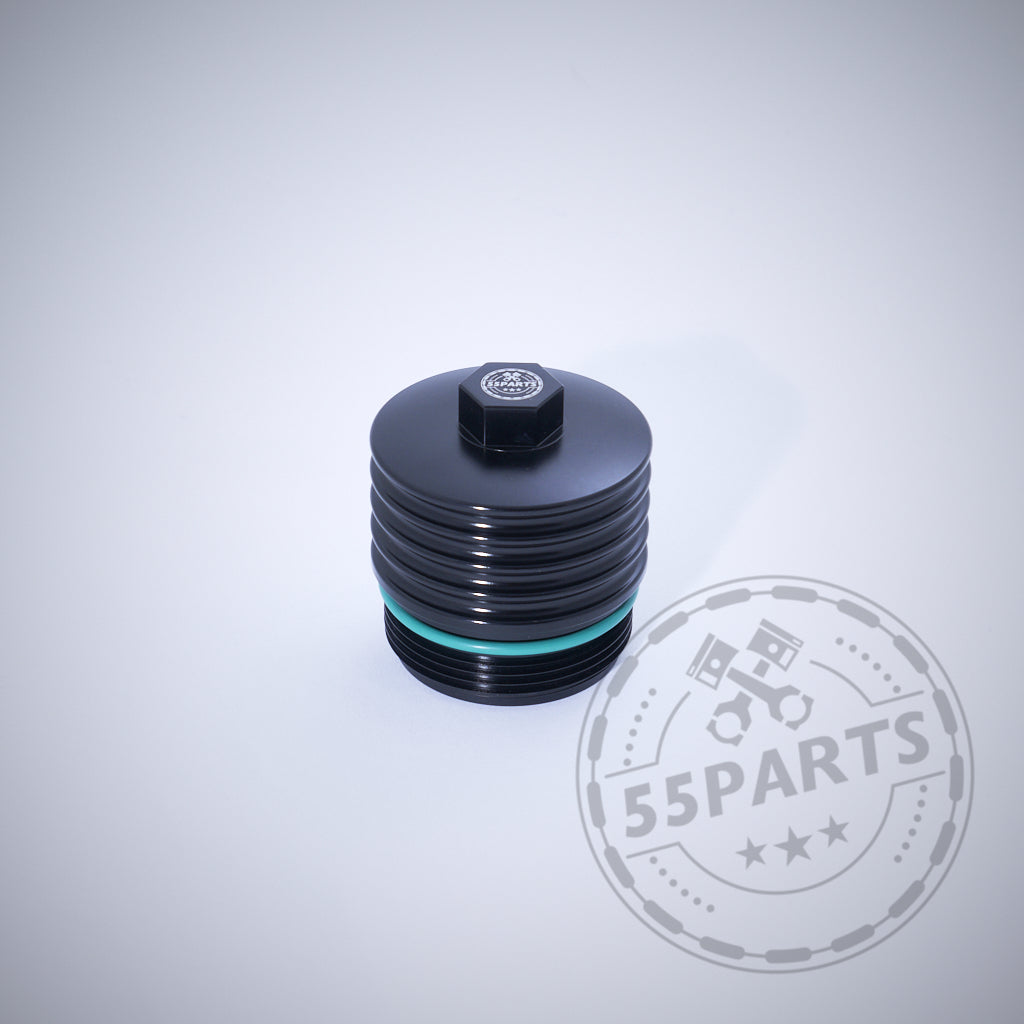 Die 55Parts Exclusive Aluminium Ölfilterkappe mit Sechskant, passend für BMW N20, N57, N52, N53, N54, N55, S55, B46, B48, B57 und B58 Motoren in schwarz mit türkisem Ring ist auf hellem Hintergrund mit 55Parts Logo abgebildet.