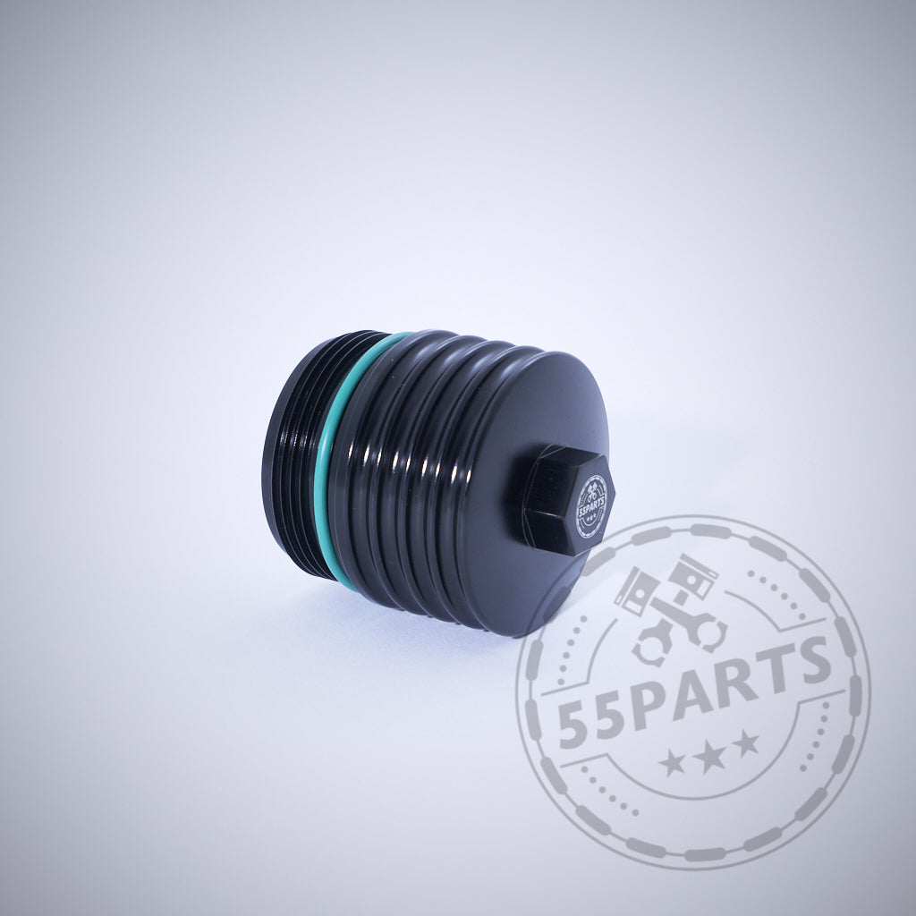 Die 55Parts Exclusive Aluminium-Ölfilterkappe mit Sechskant passend für BMW N20, N57, N52, N53, N54, N55, S55, B46, B48, B57 & B58 wird mit einem grünen O-Ring neben einem verblassten 55Parts-Logo auf hellem Hintergrund angezeigt.