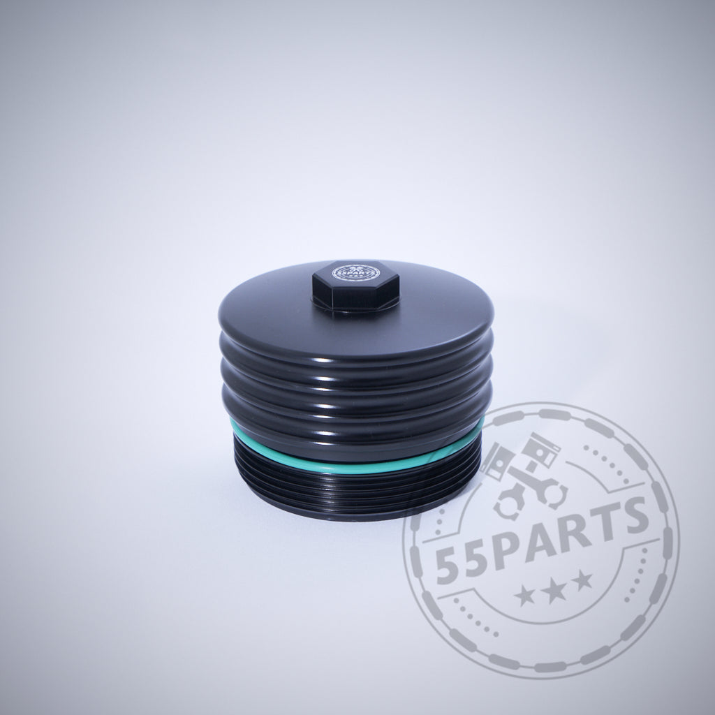 Die 55Parts Exclusive Aluminium Ölfilterkappe mit Sechskant in Schwarz mit grünem Dichtring, passend für BMW N20, N57, N52, N53, N54, N55, S55, B46, B48, B57 und B58 Motoren auf hellgrauem Hintergrund.