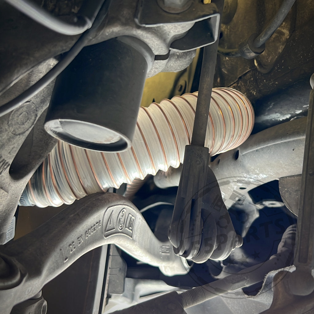 Nahaufnahme der Aufhängung eines Autos mit flexiblem Schlauch und Metallteilen, mit dem 55Parts Exclusive Bremsbelüftungsset für das BMW 2er F22 M-Paket (inkl. M235i, M240i) zur Leistungssteigerung auf der Rennstrecke.