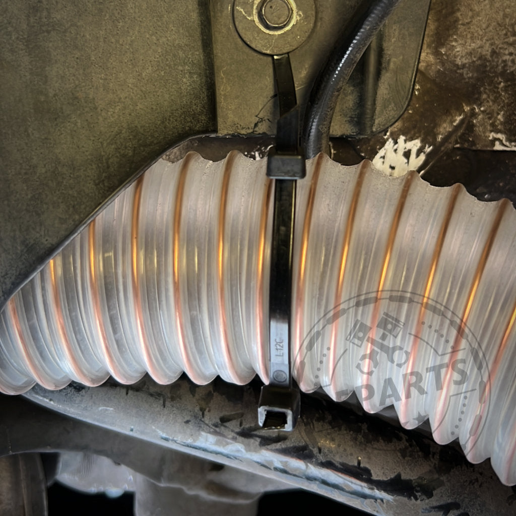 Nahaufnahme eines flexiblen Wellschlauchs mit schwarzen Kabelbindern auf einer Metalloberfläche, Teil des 55Parts Exclusive Bremsbelüftungssets passend für BMW 2er F22 mit M-Paket (z. B. M235i, M240i).