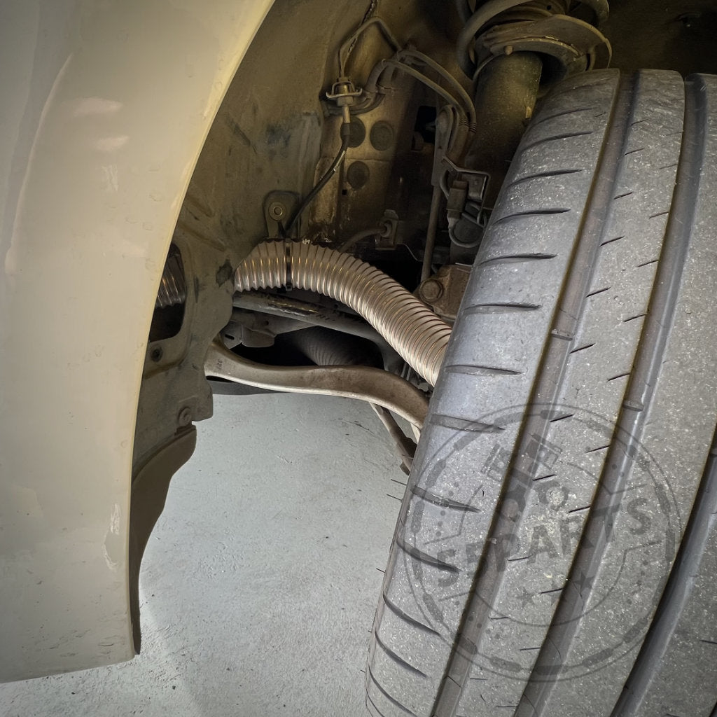 Nahaufnahme des nach außen gedrehten Vorderrads eines Autos, wodurch die Aufhängung und das 55Parts Exclusive Bremsbelüftungsset für den BMW 2er F22 mit M-Paket (inkl. M235i, M240i) sichtbar werden, das für überlegene Kühlung und Leistung auf der Rennstrecke entwickelt wurde.