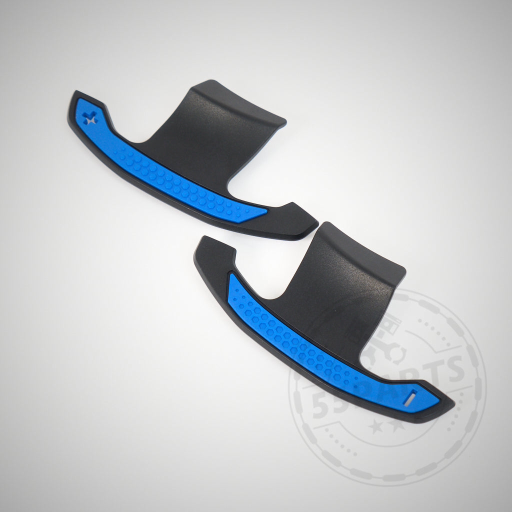 Zwei schwarze 55Parts Carbon-Schaltwippen passend für BMW 1/2/3/4 M2, M3 und M4 F- und G-Serie, abgebildet mit blauen strukturierten Griffen vor einem schlichten hellen Hintergrund.