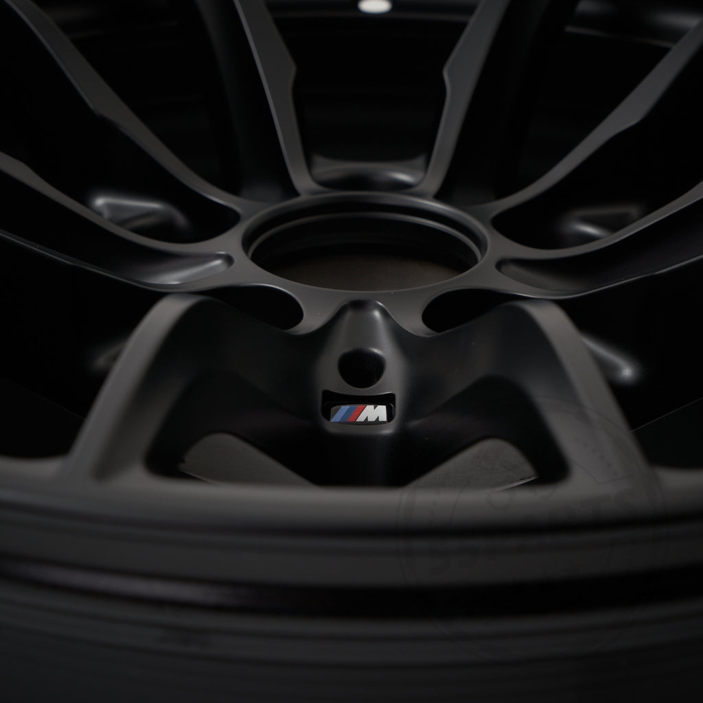 Nahaufnahme einer BMW Motorsport M2 CS Racing Felge 10,5x18 ET46 5x120 Leichtmetallfelge in Schwarz mit dem BMW M Logo in der Mitte, das den unverwechselbaren Stil von BMW Motorsport zeigt.