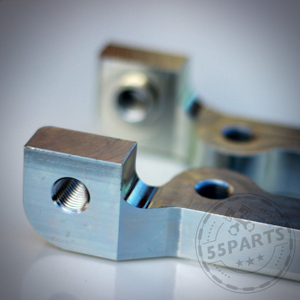 Nahaufnahme von zwei 55Parts Special: 6-Kolben Bremssatteladapter für M3 E46 CSL Scheibe, passend für BMW 1er E8x, Metallteile mit Gewindelöchern – eines scharf, das andere unscharf – zeigen Präzisionstechnik.