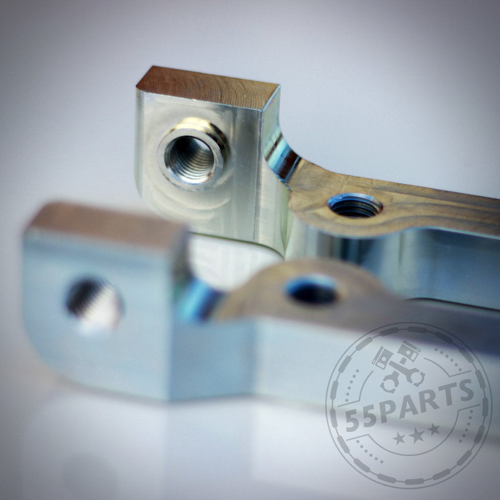 Nahaufnahme von zwei 55Parts Special: 6-Kolben Bremssatteladapter für M3 E46 CSL Scheibe, passend für BMW 1er E8x, Metallteile mit Gewindelöchern – eines scharf, das andere unscharf – zeigen Präzisionstechnik.