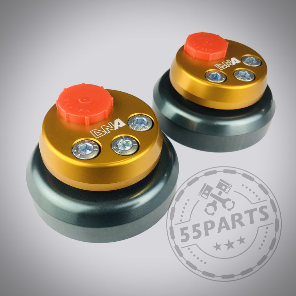 Auf grauem Hintergrund sind zwei gold-schwarze verstellbare Uniball-Domlager von DNA Racing mit roten Knöpfen und silbernen Schrauben abgebildet – ideal für Besitzer eines Toyota Yaris GR, die Premium-Tuningteile für eine verbesserte Leistung wünschen.