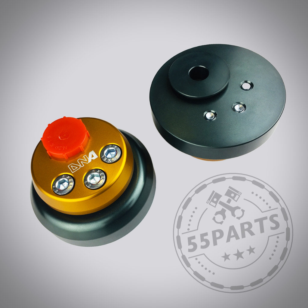 DNA Racing Verstellbares Uniball Domlager passend für Toyota Yaris GR: Zwei runde Teile, eines gold-schwarz mit Schrauben, eines schwarz, auf grauem Hintergrund mit Tuning Shop Logo. Ideal für Yaris GR-Fans für mehr Fahrspaß.