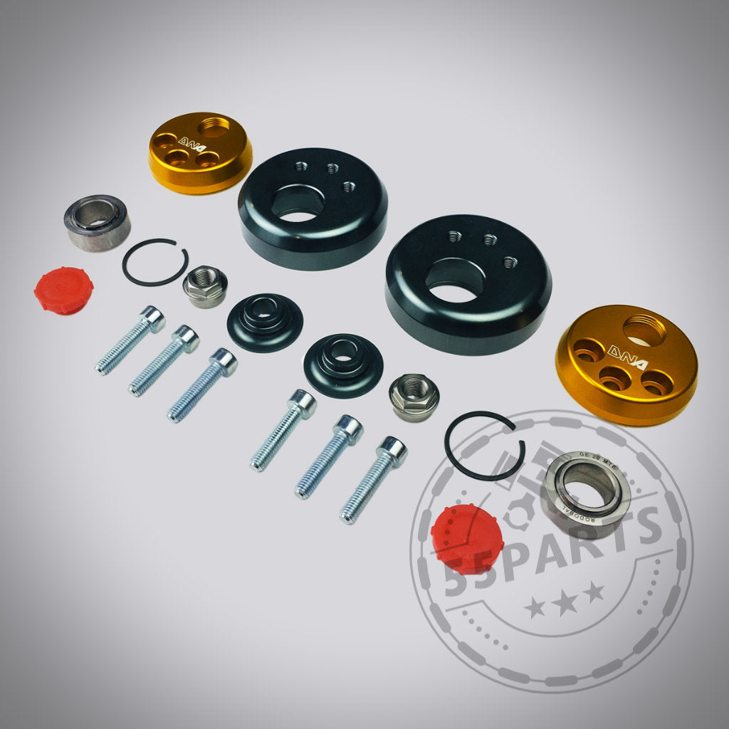 DNA Racing Verstellbares Uniball Domlager für Toyota Yaris GR inklusive Metallbolzen, Unterlegscheiben, Lager sowie orange-schwarzer Rundteile für Fahrwerkstuning – arrangiert auf grauem Hintergrund.