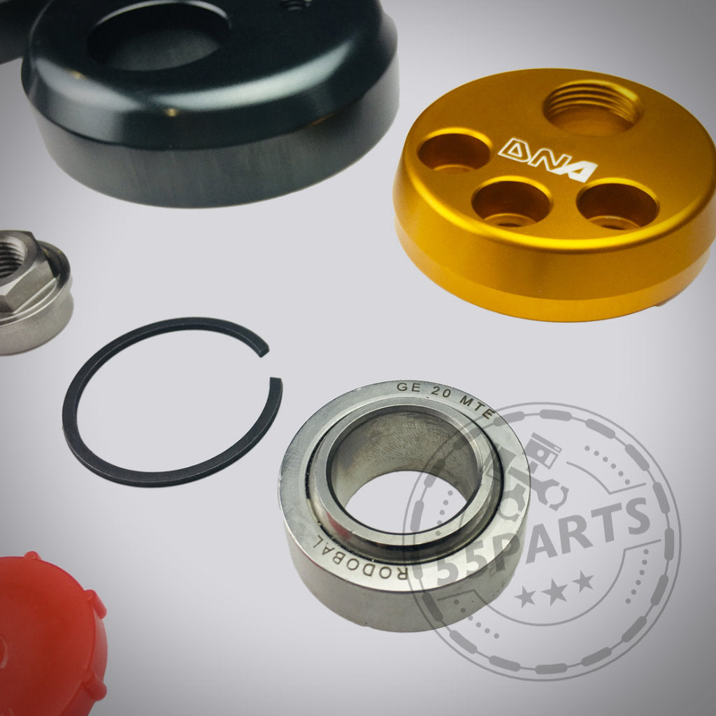 Das verstellbare Uniball-Domlager von DNA Racing für den Toyota Yaris GR umfasst verschiedene Metall- und Kunststoffteile wie ein Lager, Ringe und ein goldenes Rundstück – ideal für Tuningprojekte mit Ihrem Yaris GR-Fahrwerk.