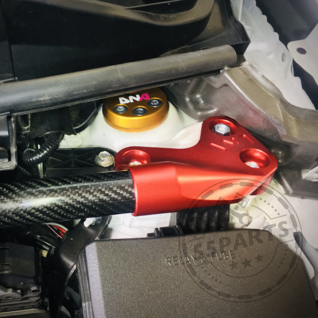 Nahaufnahme eines verstellbaren Uniball-Domlagers von DNA Racing, einer präzisen Federbeinhalterung aus rotem Metall mit sichtbaren Schrauben und Kohlefaserrohr, eingebaut im Motorraum eines Toyota Yaris GR.