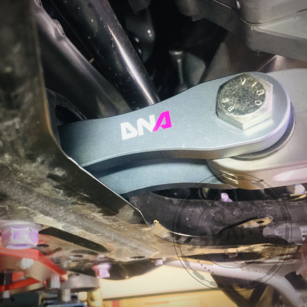 Nahaufnahme eines metallischen Autoaufhängungsteils mit einer Schraube mit der Aufschrift „DNA“. Das DNA Racing Upgrade Drehmoment Stütze Motorlager ist ideal für Toyota Yaris GR-Besitzer, die sich von DNA Racing eine verbesserte Leistung wünschen.