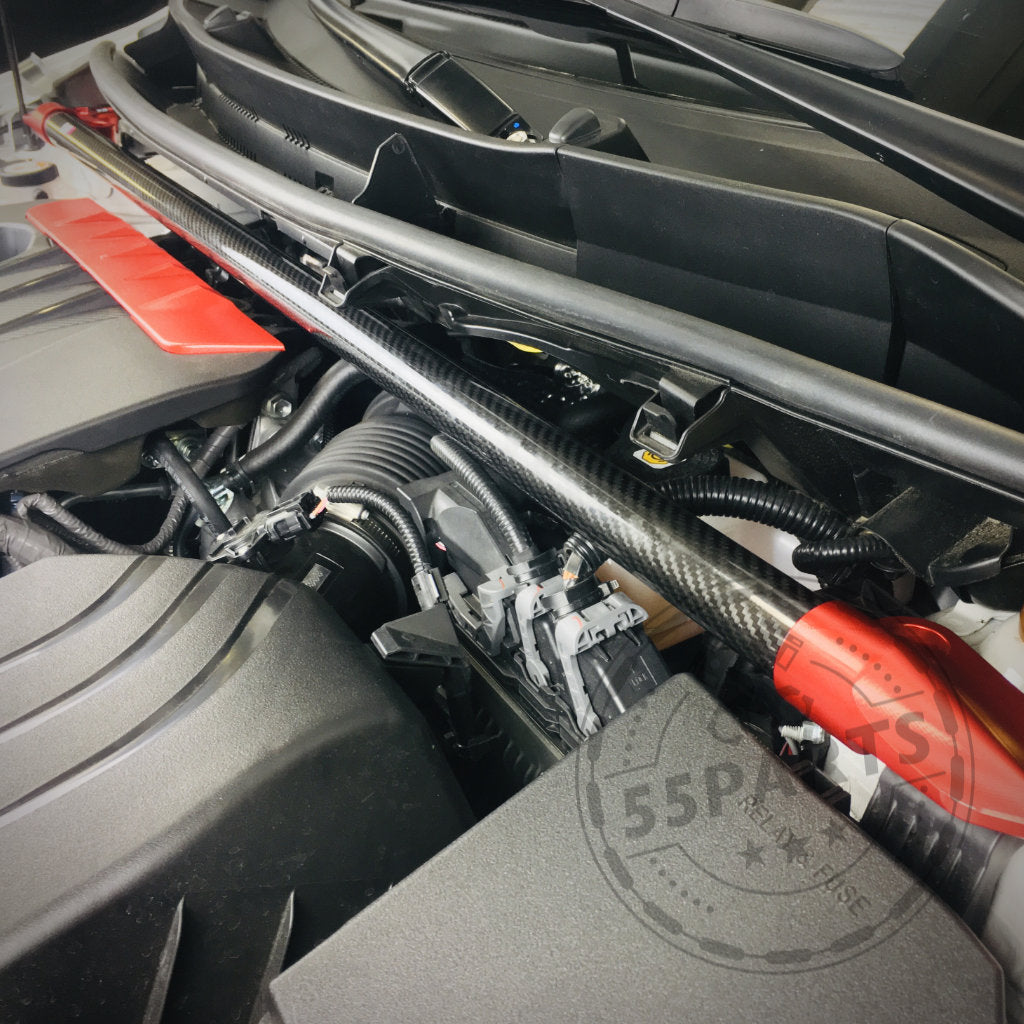 Nahaufnahme eines Motorraums eines Toyota Yaris GR, der mit einer DNA Racing Carbon-Domstrebe vorne ausgestattet ist. Hervorzuheben sind die Domstrebe aus Carbonfaser und die rote Motorabdeckung der Premium-Tuning-Marke DNA Racing.