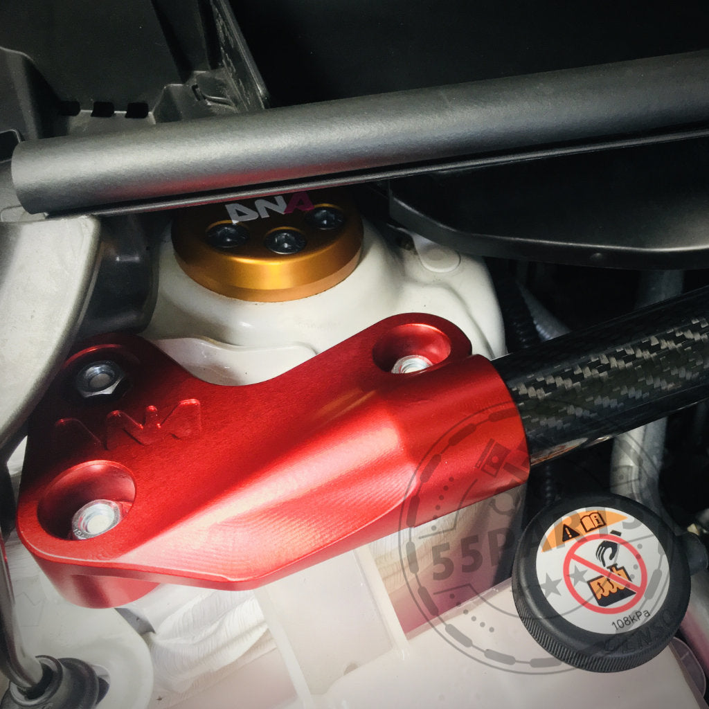 Nahaufnahme eines roten Metallmotorteils mit Schrauben, einer DNA Racing Carbon-Domstrebe vorne und einem Warnschild, das die Präzision der DNA Racing-Upgrades für den Toyota Yaris GR hervorhebt.