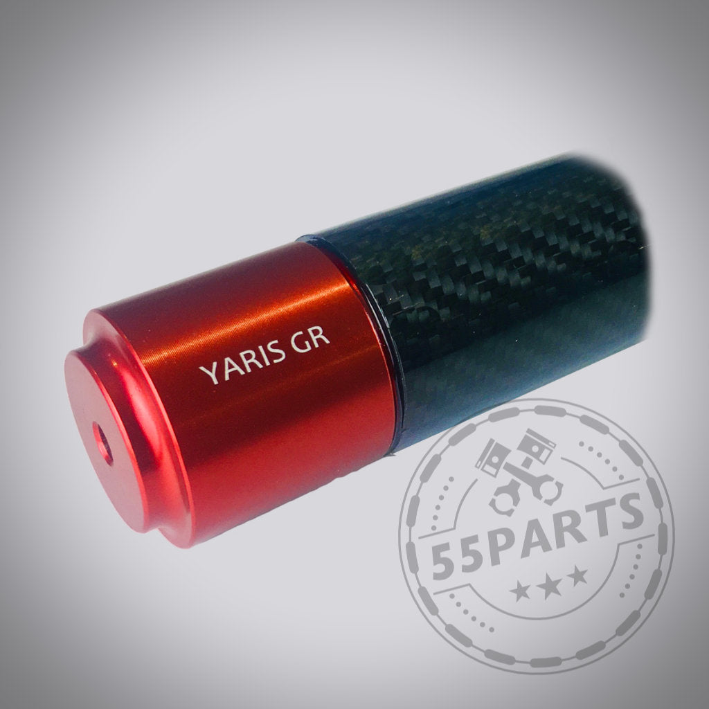 Schwarze Carbon-Hinterradstrebe von DNA Racing für den Toyota Yaris GR mit roten Endkappen. Abgebildet auf hellgrauem Hintergrund mit dezentem Wasserzeichen. Perfekt für Yaris GR-Besitzer oder Upgrades im Toyota Tuning Shop.