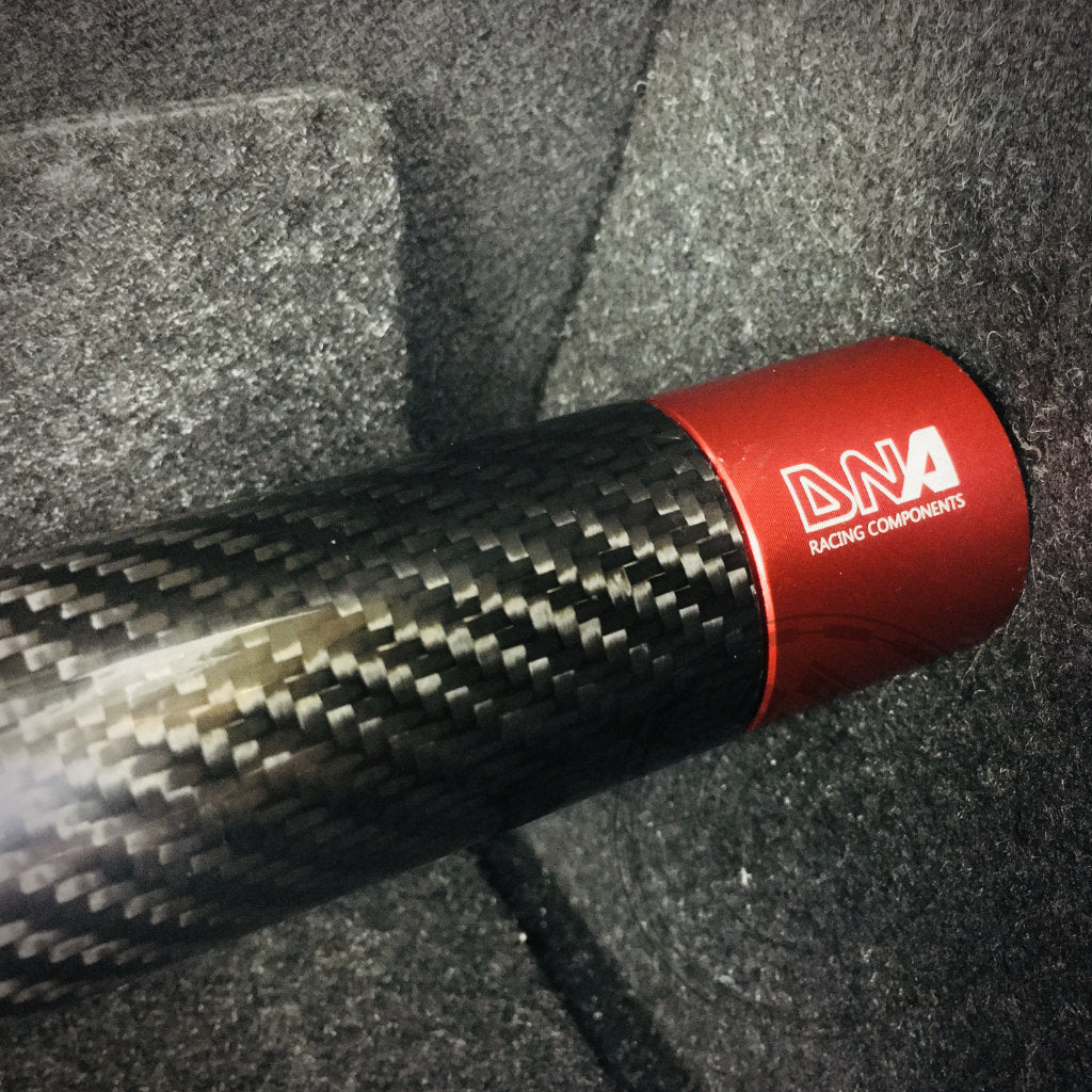 Nahaufnahme der DNA Racing Carbon Domstrebe hinten für den Toyota Yaris GR, mit einer roten Endkappe mit DNA Racing-Branding – ein unverzichtbares Upgrade für Yaris GR-Fans, jetzt erhältlich in Ihrem bevorzugten Tuning-Shop.