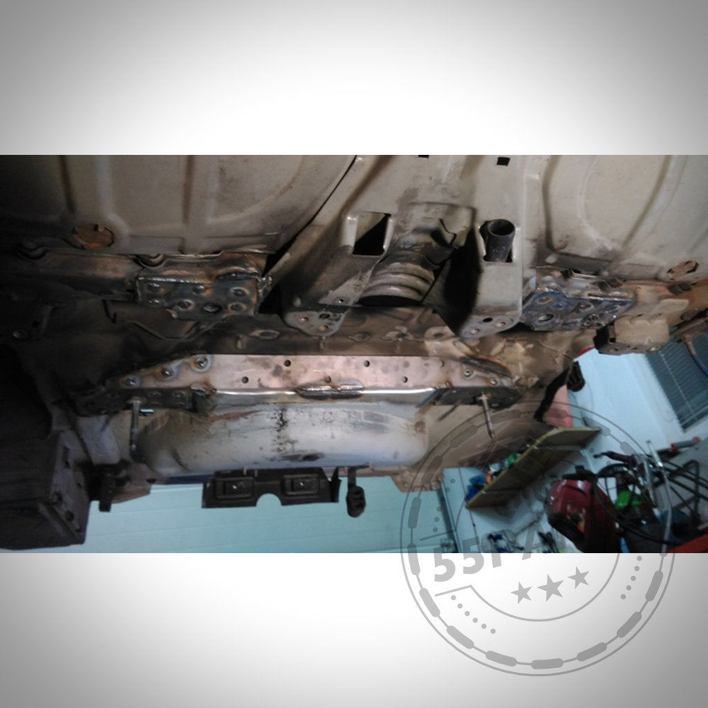 Ansicht eines BMW 3er E46 in einer Werkstatt mit eingebauten 55Parts-Verstärkungsblechen Hinterachse, die geschweißte Metallverstärkungen, Modifikationen an Aufhängung und Hinterachse sowie Auspuffkomponenten zeigen.