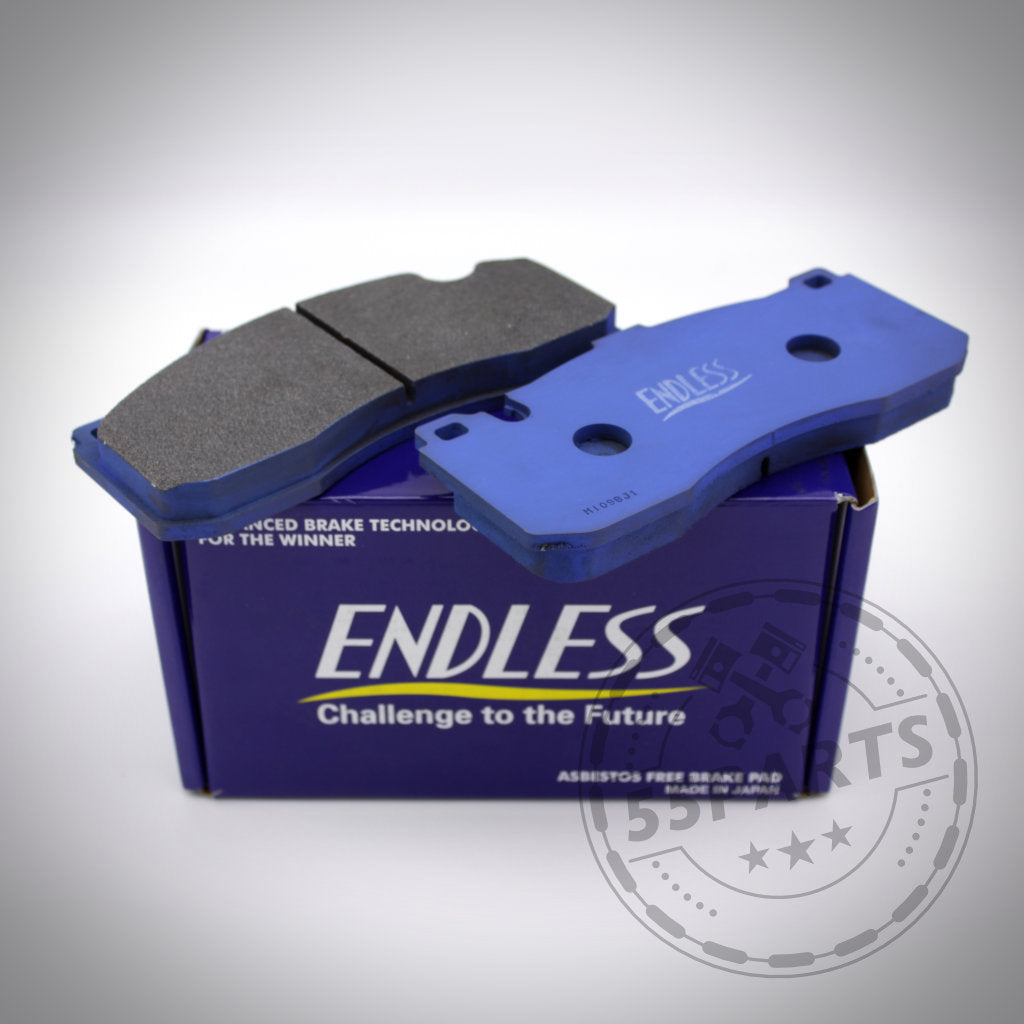 Zwei blaue Endless-Bremsbeläge für 6-Kolben BMW (Performance) Sattel, passend für BMW 135i E82/E88, ruhen auf einer lila Endless-Box mit kreisförmigem Stempellogo – ideal für BMW-Fans.