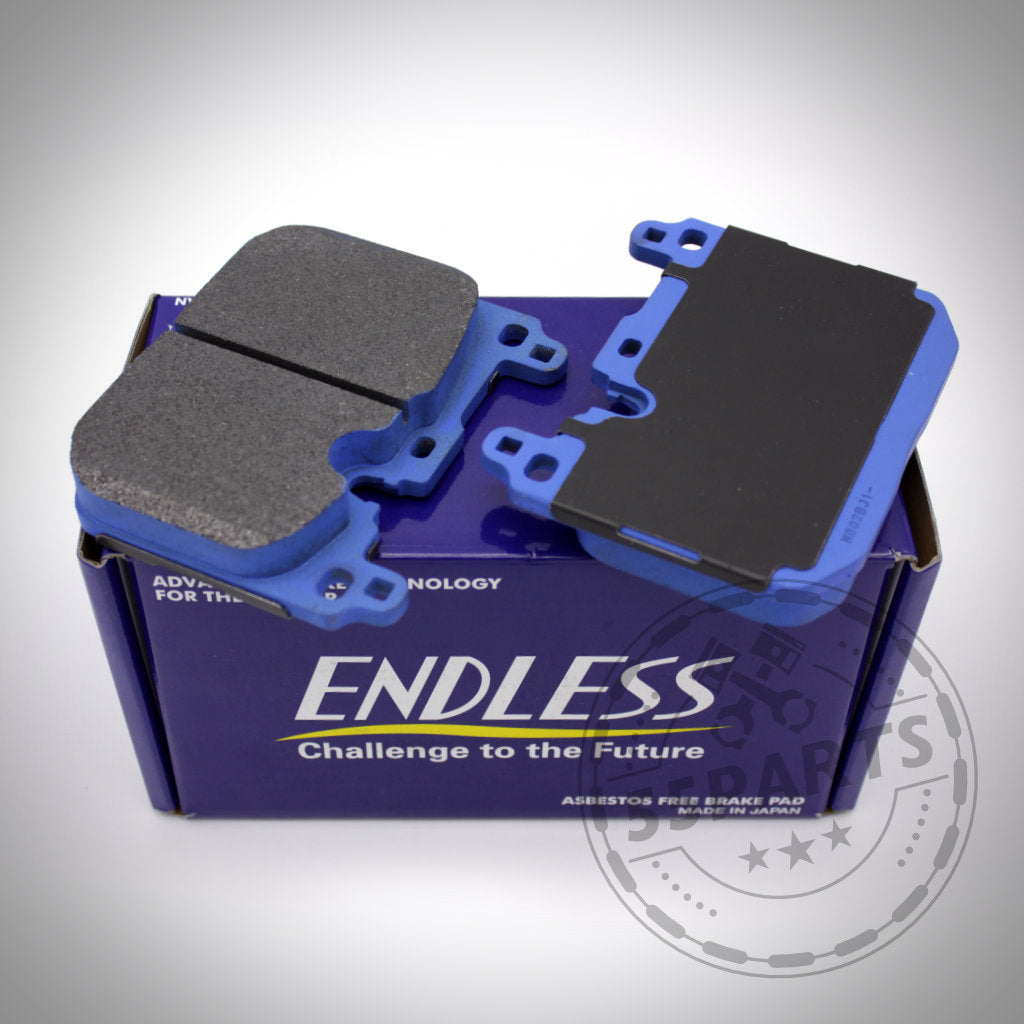 Zwei blaue und schwarze Endless-Bremsbeläge für Blaue 4-Kolben/2-Kolben-Anlage (ohne Keramik) sitzen auf einer lila Endless-Box, perfekt für die Rennstrecke oder die Aufrüstung von BMW M135i/40i, M235i/40i, 335i/40i, 435i/40i, M2, M3 & M4 (F-Serie).