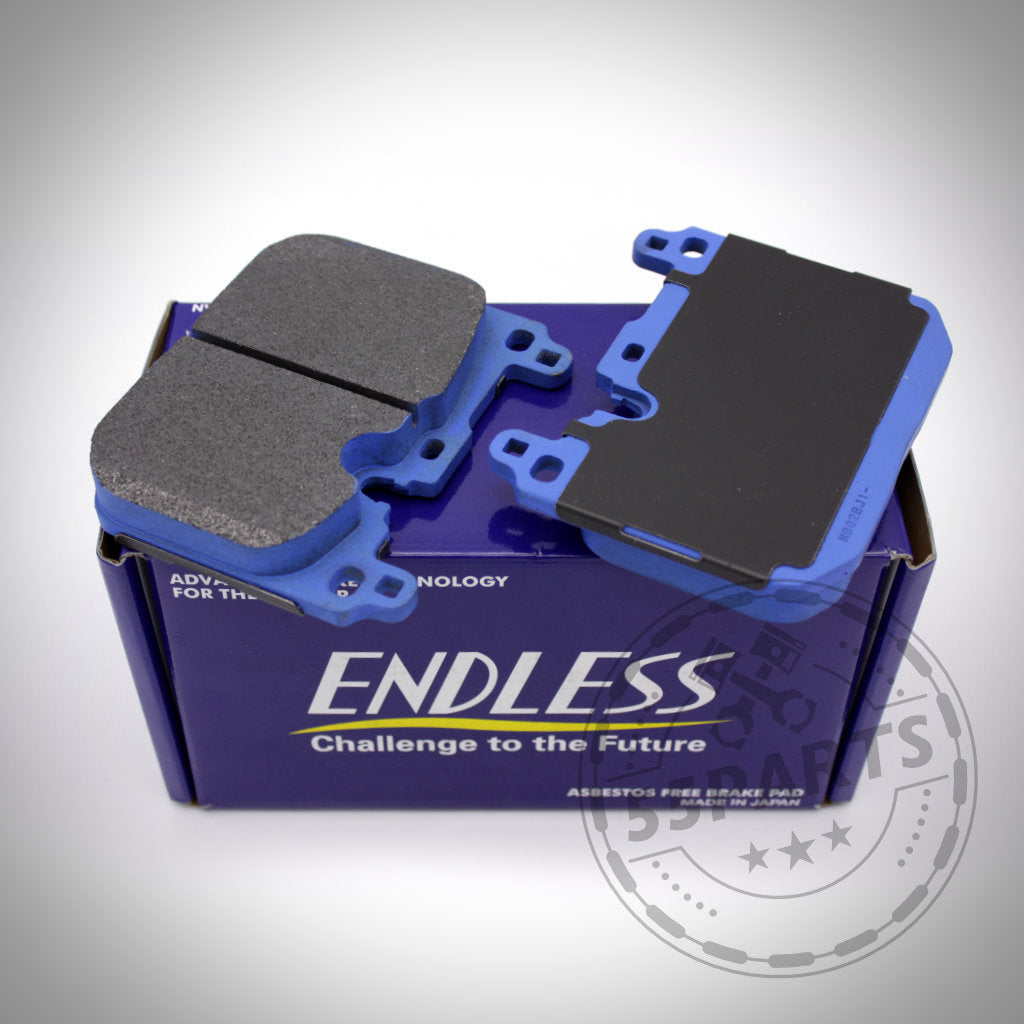 Zwei blaue und schwarze Endless-Bremsbeläge für Blaue 4-Kolben/2-Kolben-Anlage (ohne Keramik) sitzen auf einer lila Endless-Box, perfekt für die Rennstrecke oder die Aufrüstung von BMW M135i/40i, M235i/40i, 335i/40i, 435i/40i, M2, M3 & M4 (F-Serie).