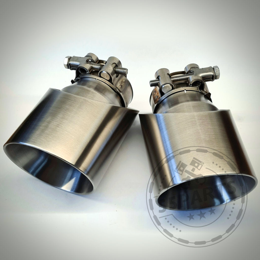 Zwei 55Parts Spezial-Endrohrblenden für F22, F23, F30-F36 x35i/x40i mit Klemmen, auf einer hellen Fläche platziert und aus einem Winkel betrachtet.