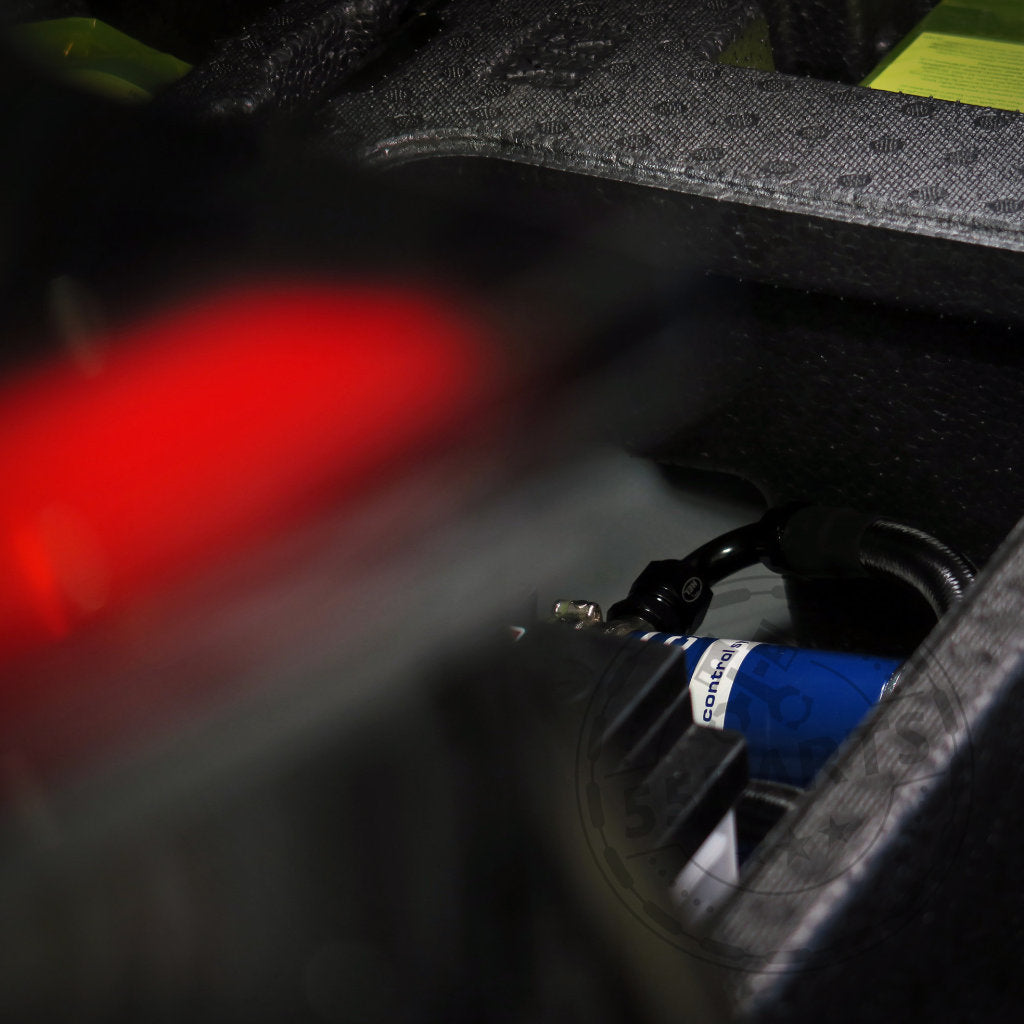 Nahaufnahme eines Fachs mit aufgerollten Kabeln und Ausrüstung, teilweise verdeckt durch ein rotes, verschwommenes Objekt im Vordergrund, mit dem HEL Performance Plug and Play Differential-Kühlungskit Hinterachse für GR Yaris Special.