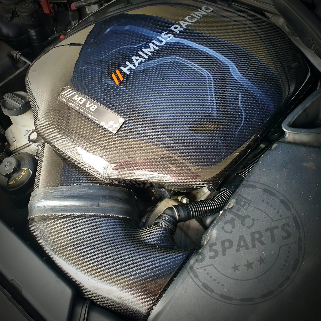 Nahaufnahme des 55Parts Special: Haimus Racing Carbon-Luftsammler, entworfen passend für BMW E9x M3, beschriftet mit S65 V8 und M5 V8, eingebaut im Motorraum.