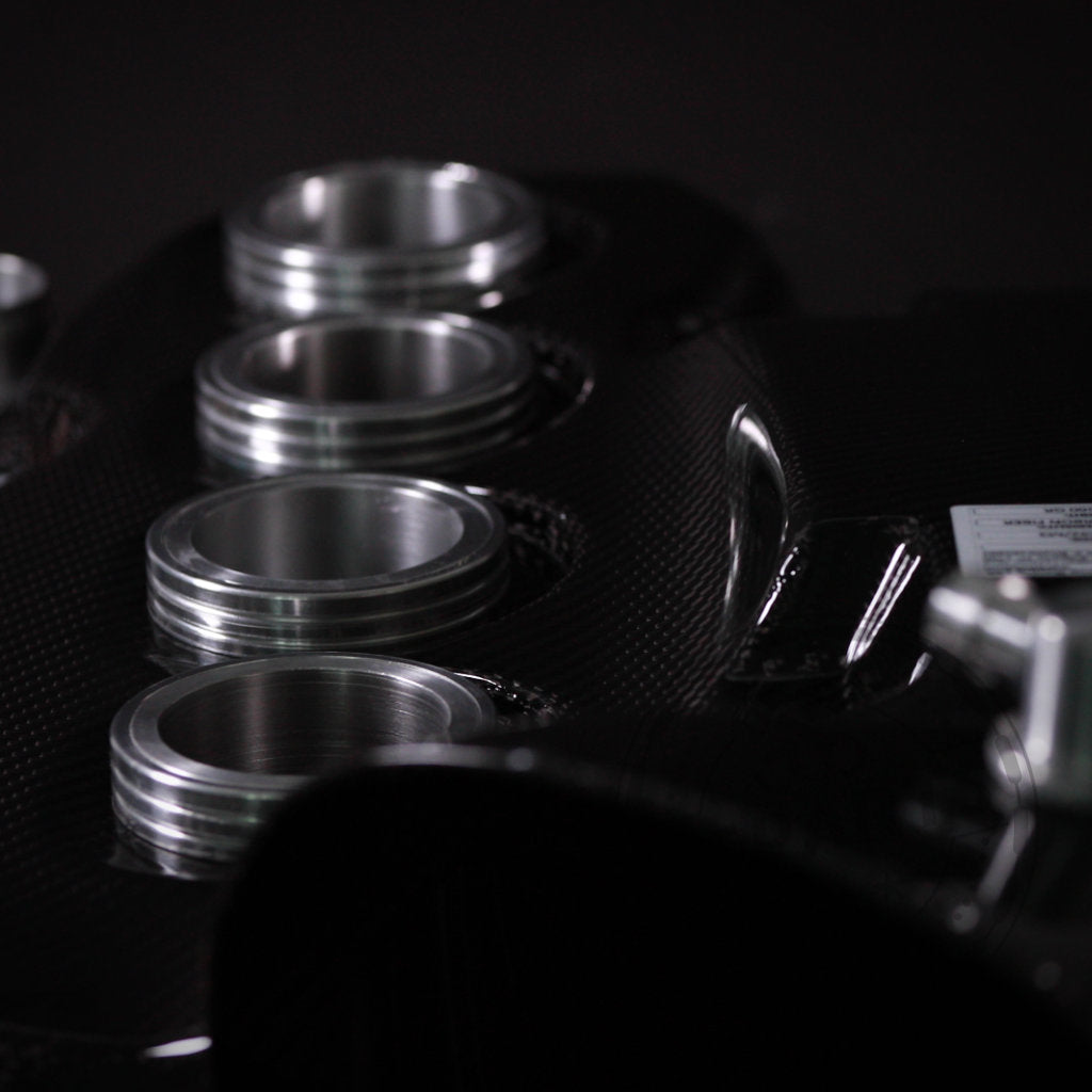 Nahaufnahme von vier Ansaugstutzen aus Metall auf einem 55Parts Special: Haimus Racing Carbon-Luftsammler passend für BMW E9x M3, vor einem dunklen Hintergrund.