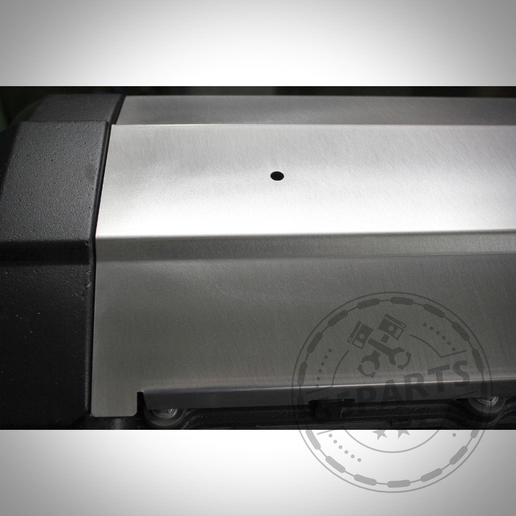 Nahaufnahme des 55Parts Hitzeschutzblechs für Ventildeckel, entwickelt für die BMW-Motoren M50B25, M52B20 und B52B28 – ein Metallschild mit einem kleinen Loch, teilweiser schwarzer Kunststoffkante und einem Logo-Wasserzeichen in der Ecke.