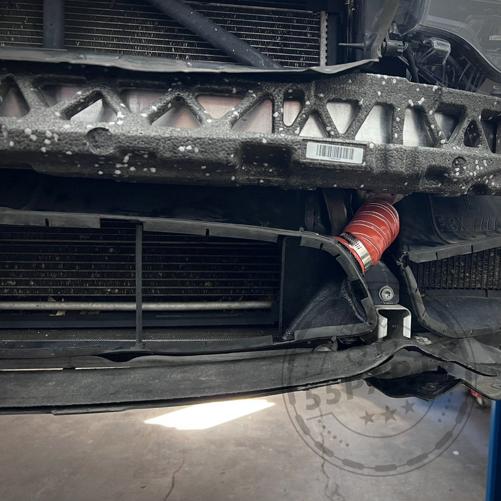 Nahaufnahme eines BMW M3/M4 F8x mit beschädigter Stoßstange, Kühlergrill, freiliegendem Kühler und rotem Schlauch – mit dem exklusiven Bremsbelüftungsset, was auf kürzlich erfolgte Upgrades auf der Rennstrecke schließen lässt.