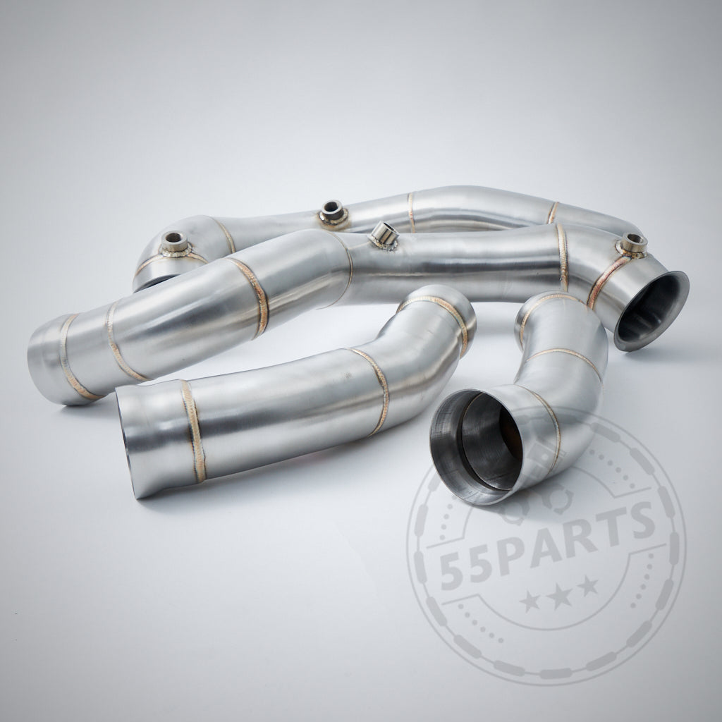 Zwei metallische High Flow 3,5" Downpipes, passend für Mercedes Benz AMG C63(S) W205 M177, mit verschweißten Nähten, liegen auf einer hellgrauen Oberfläche. Geeignet als Catless oder mit 200-Zellen-Kat.