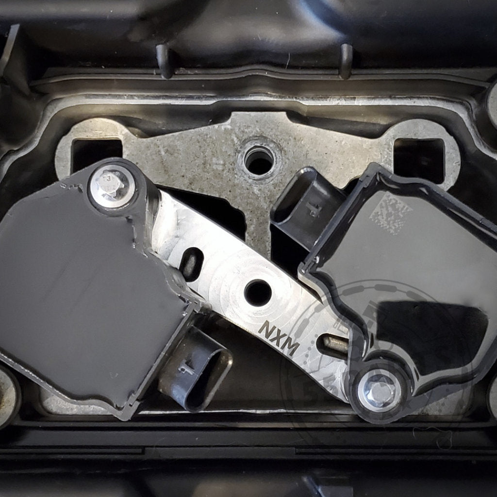 Nahaufnahme eines schwarz-silbernen Motorteils mit der Gravur NXM, mit dem NexSys B58 Zündspulen-Upgrade-Kit von Nexsys Motorsport, das für die BMW S55- und N55-Motoren (E8x, E9x, F2x, F3x, F8x) zur Leistungssteigerung entwickelt wurde.