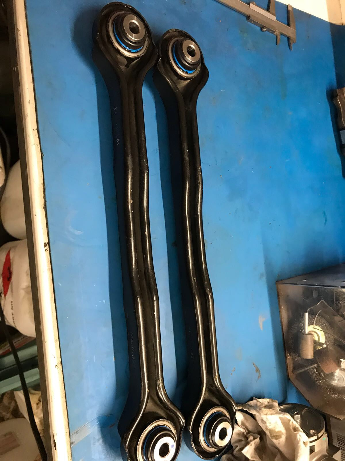 Zwei schwarze NoFlex-Lager – Kugelgelenksatz für originalen Spurlenker und Längslenker – liegen nebeneinander auf einer blauen Werkbank, ideal für Fahrwerks-Upgrades passend für BMW 1er E8x und 3er E9x.