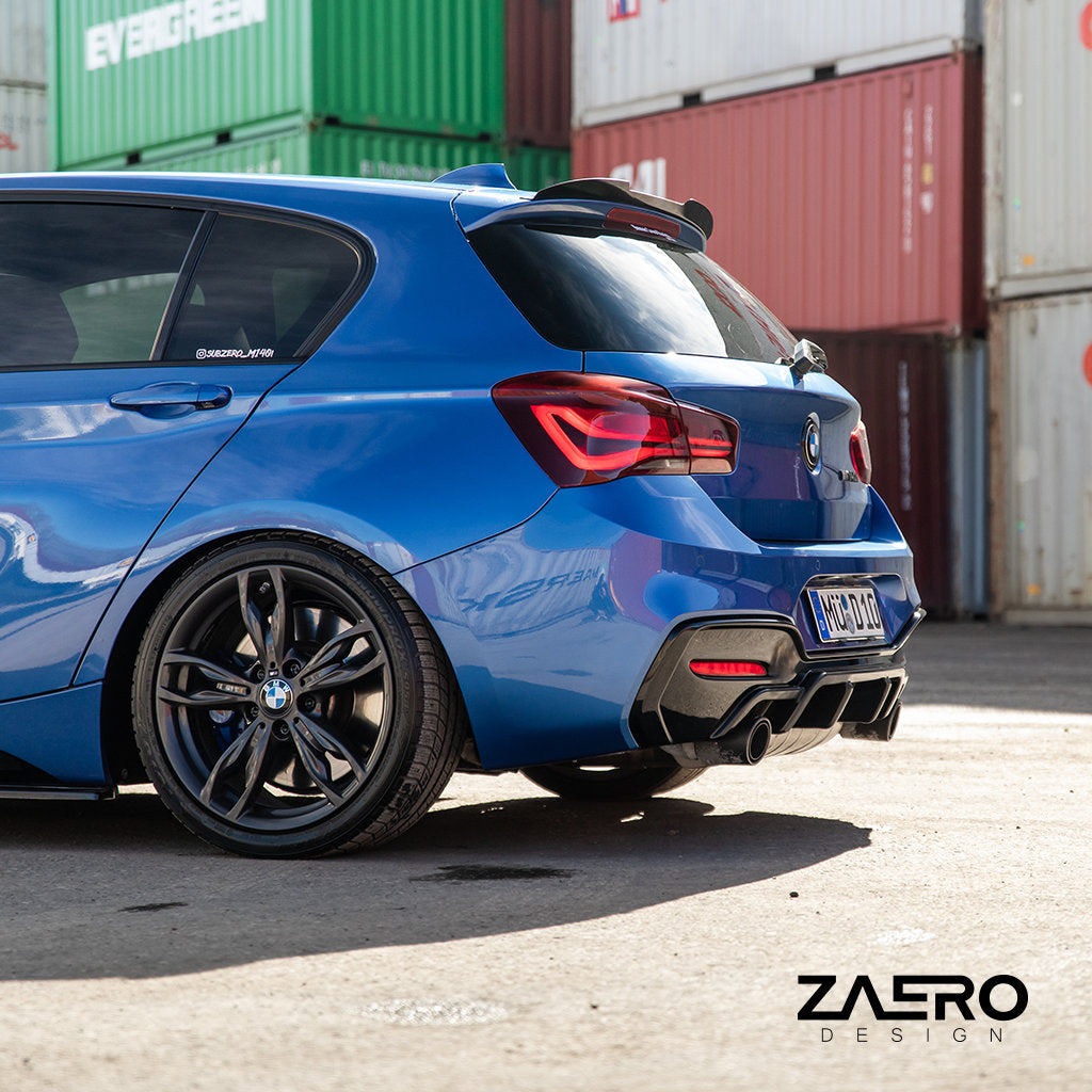 Ein blauer BMW M135i/M140i F2x mit ZAERO Evo-1 Diffusor und Carbon-Anbauteilen fährt in einem Industriegebiet an gestapelten Schiffscontainern vorbei, von hinten gesehen.